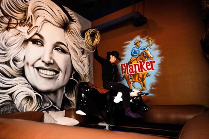 Guest riding a mechanical bull in front of Flanker cowboy mural and large Dolly Parton wall art