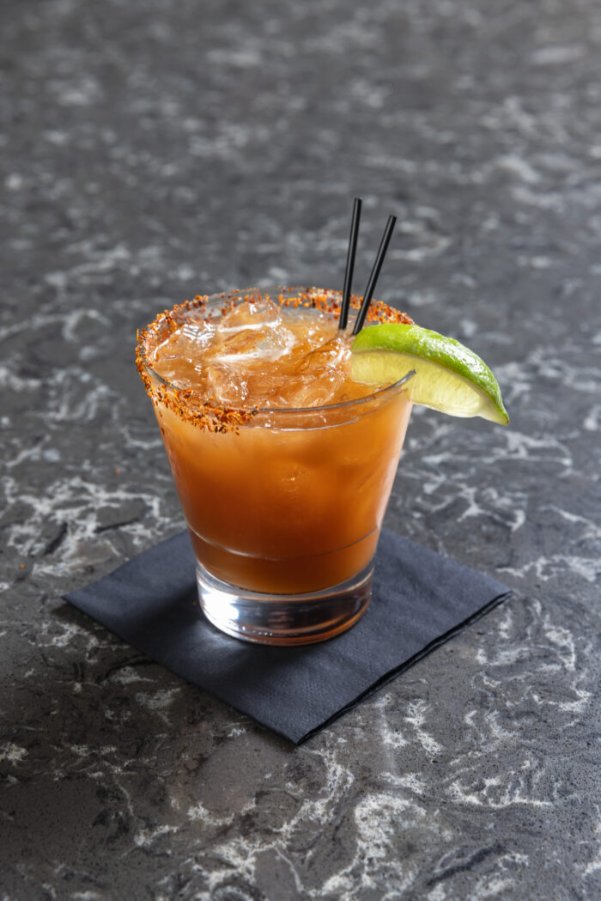 Spicy cocktail with chili-salt rim, lime wedge garnish, and ice served on a black napkin Spicy chili-rim cocktail with lime garnish