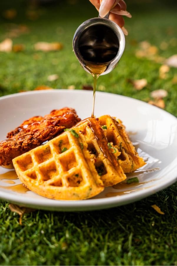 Chicken and waffles topped with maple syrup being poured over the dish