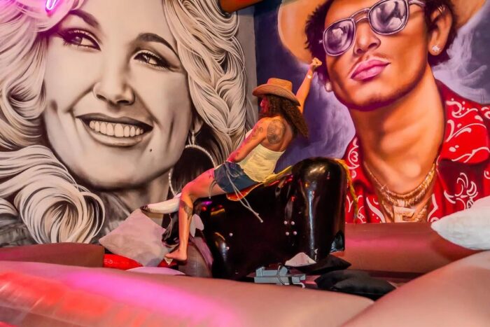 Image pop-up Person riding a mechanical bull in front of colorful Western-themed murals.