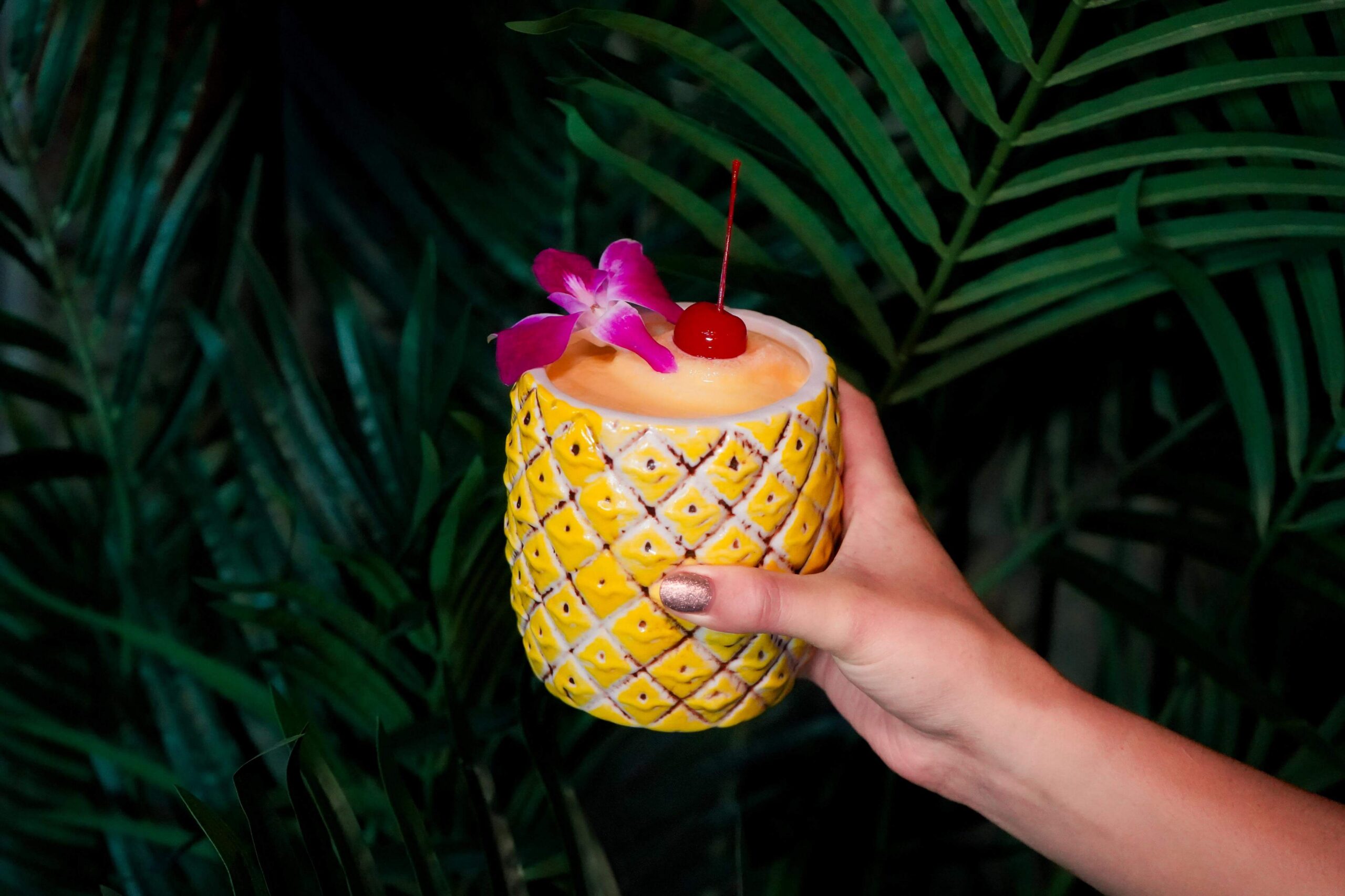 Tropical frozen cocktail served in a yellow pineapple-shaped glass and garnished with an orchid and cherry.